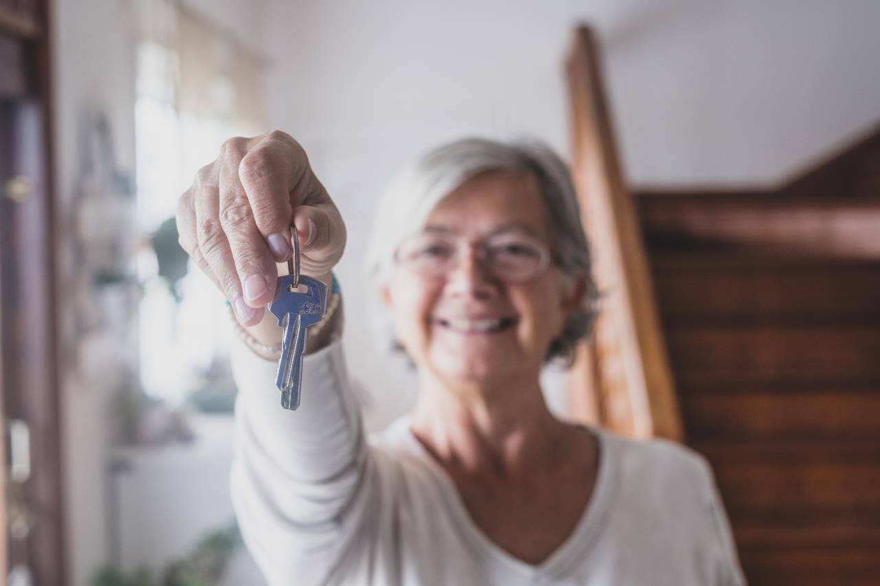Zu sehen ist eine zufriedene Seniorin die einen Hausschlüssel hält